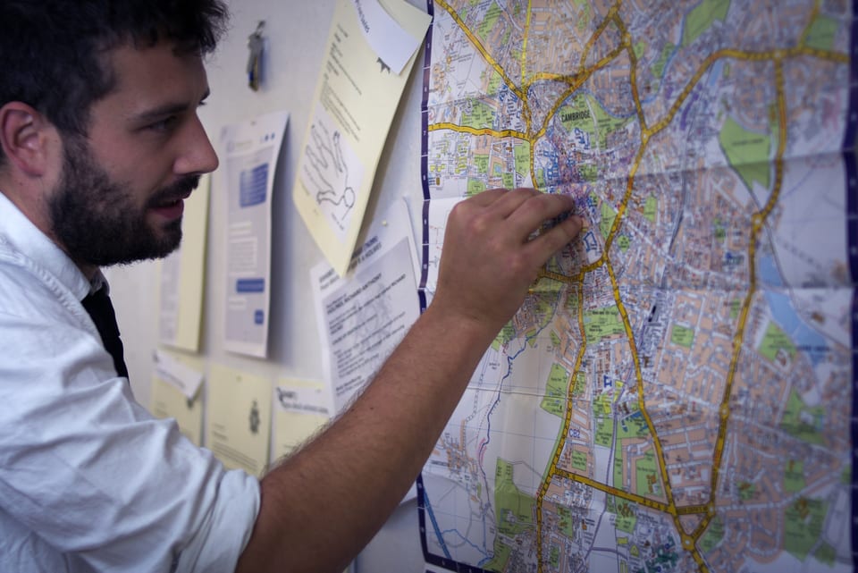 An investigator examines a Cambridge map and case documents on an evidence wall.